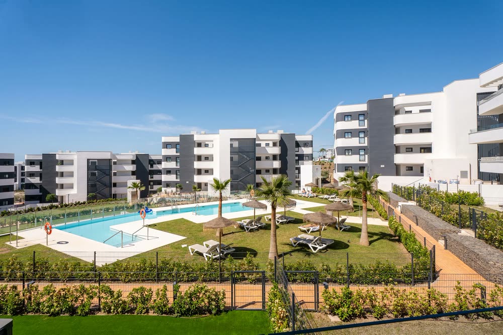 Apartment complex with a landscaped pool and gardens under a blue sky