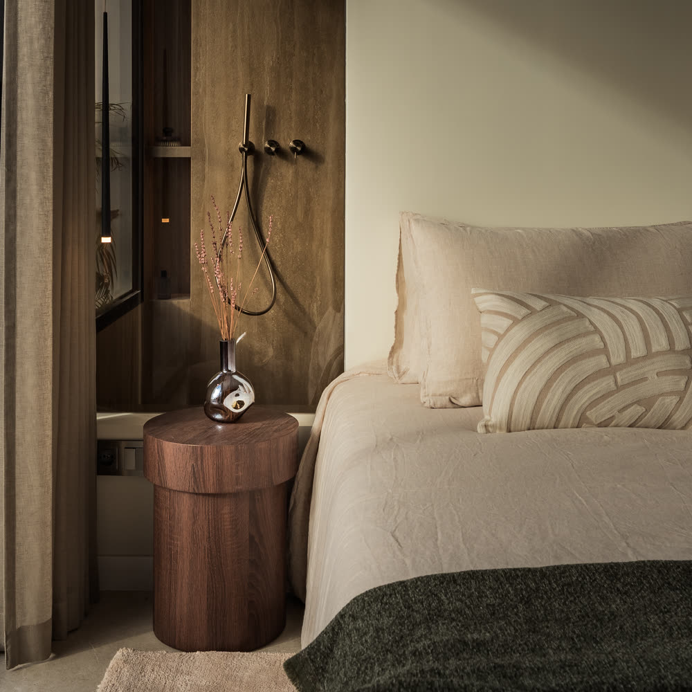 Bedside with a round walnut table and dried lavender against a travertine wall